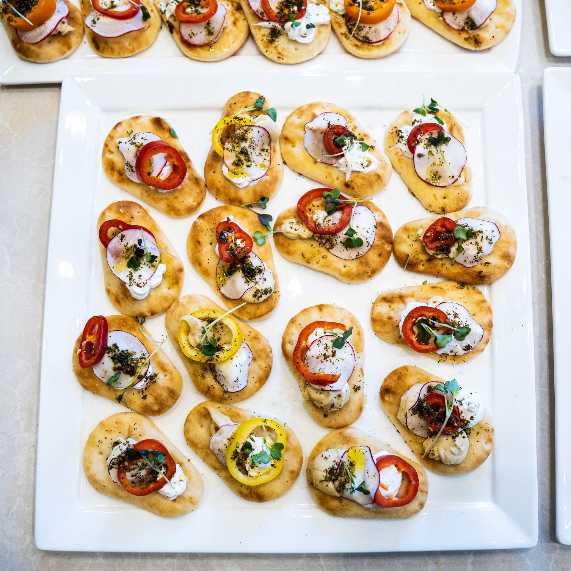 Mini flatbread canapés topped with labneh, radish, peppers and microgreens