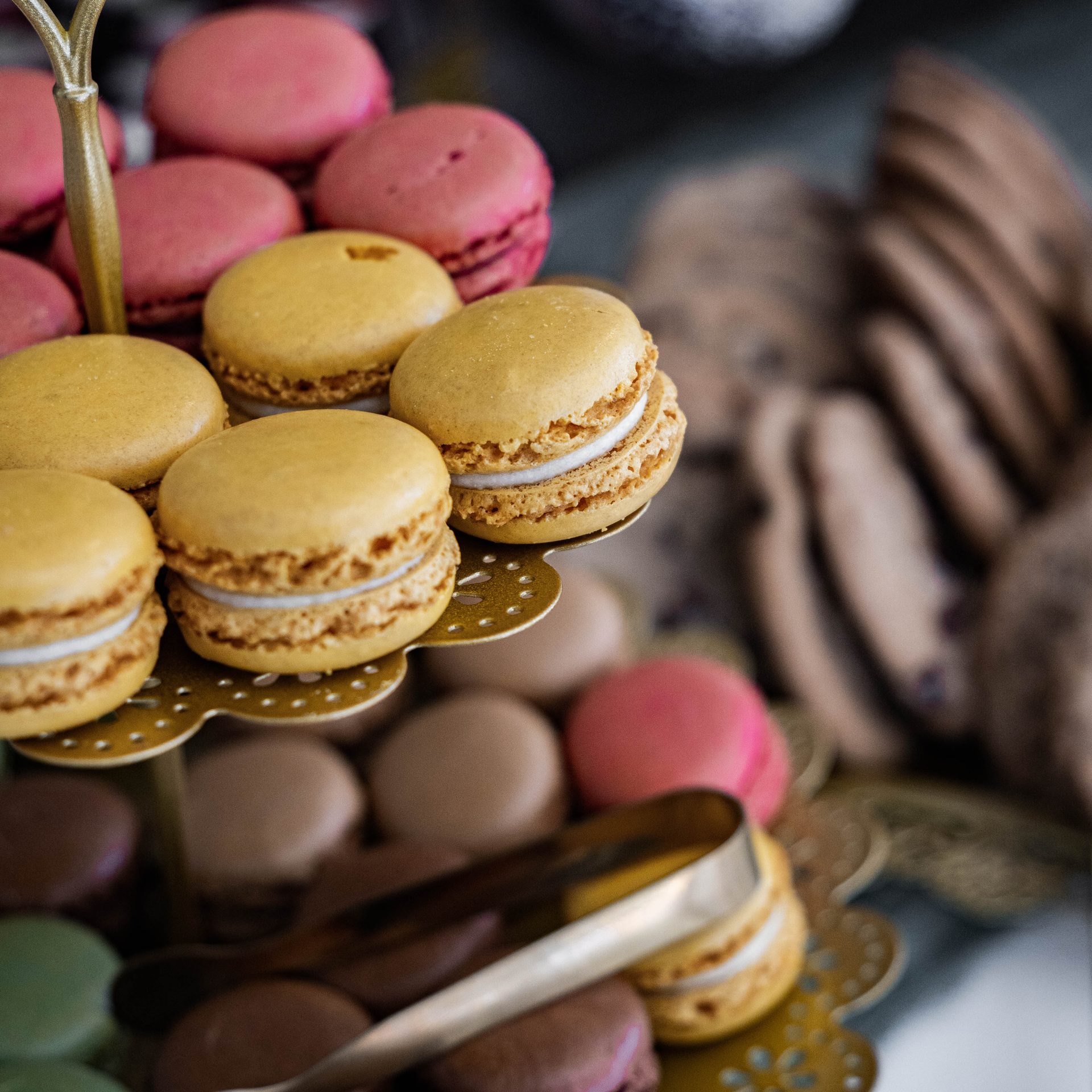 Caramel and rose macarons with cookies on a gold dessert stand