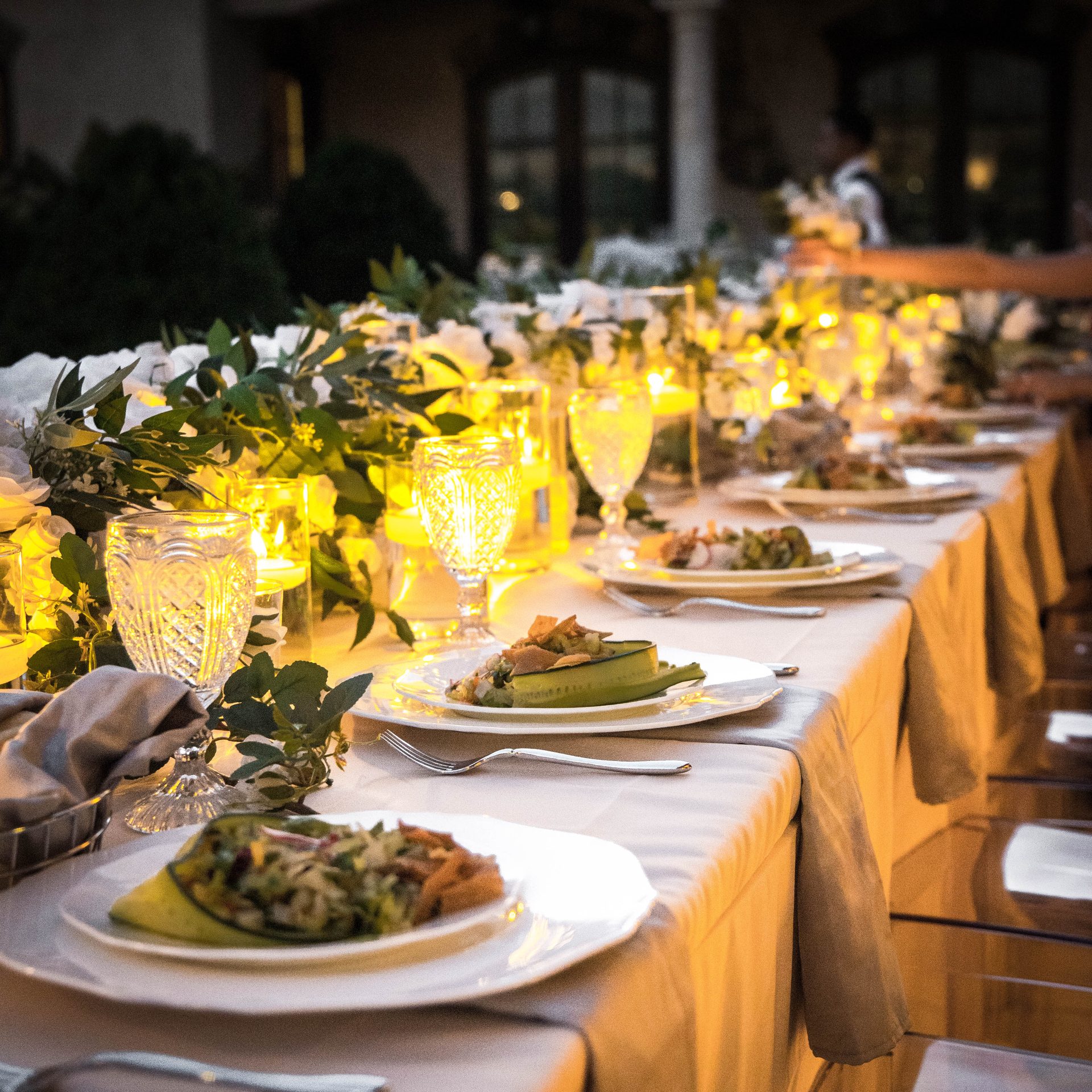 Long candlelit banquet table set with plated Lebanese food and greenery garland